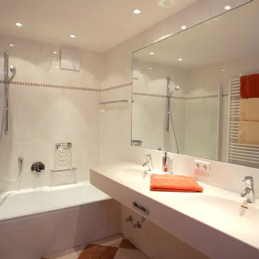 Engenkopf Modern bathroom with double sink, bathtub, wall mirror, and orange towels